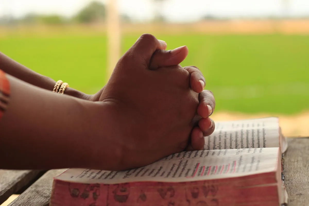 Hands clasped in prayer over an open Bible