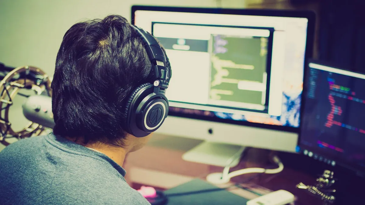 Programmer wearing headphones writing code on dual monitors