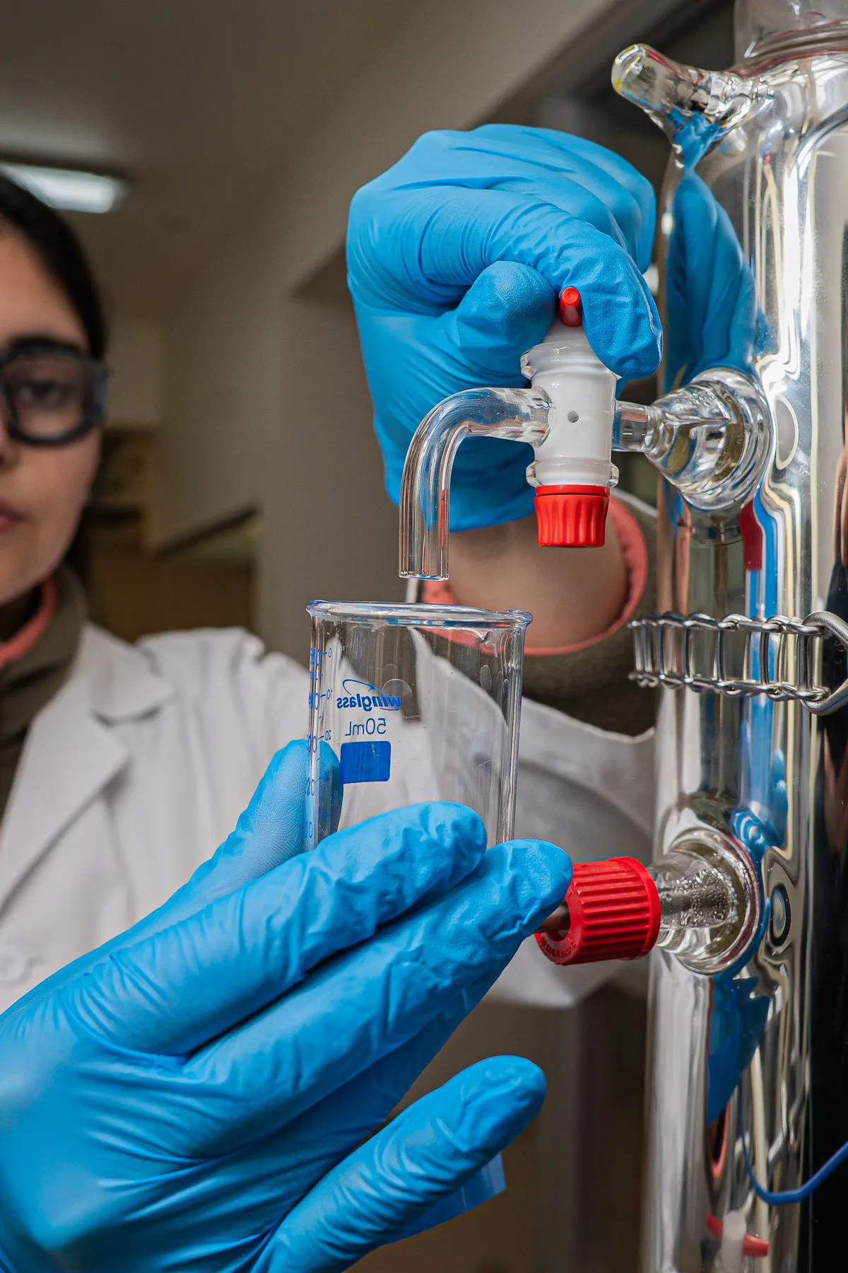 Scientist in gloves and goggles adjusting a distillation apparatus in a lab